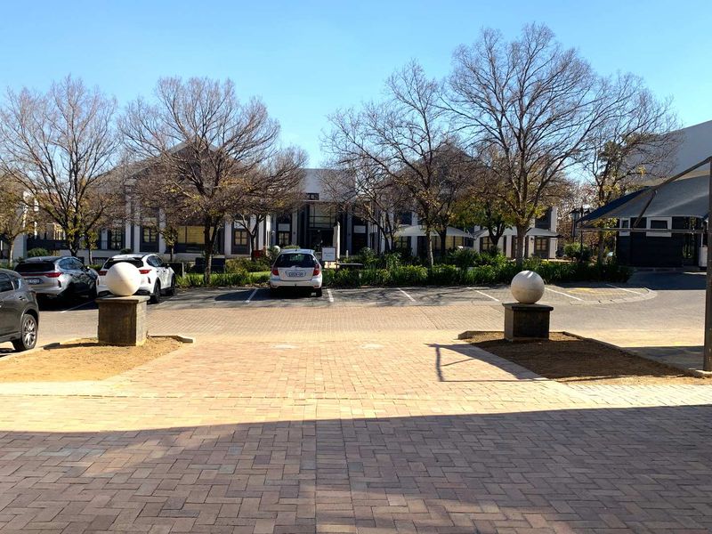 A view of the office complex exterior featuring a paved entrance, parking area, and well-maintained landscaped grounds.