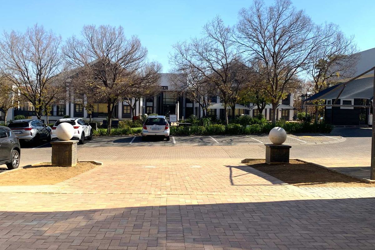 A view of the office complex exterior featuring a paved entrance, parking area, and well-maintained landscaped grounds.