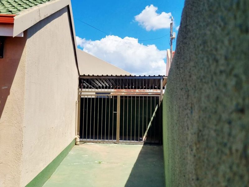 A narrow side passage featuring a concrete driveway, enclosed by a metal security gate and a perimeter wall.
