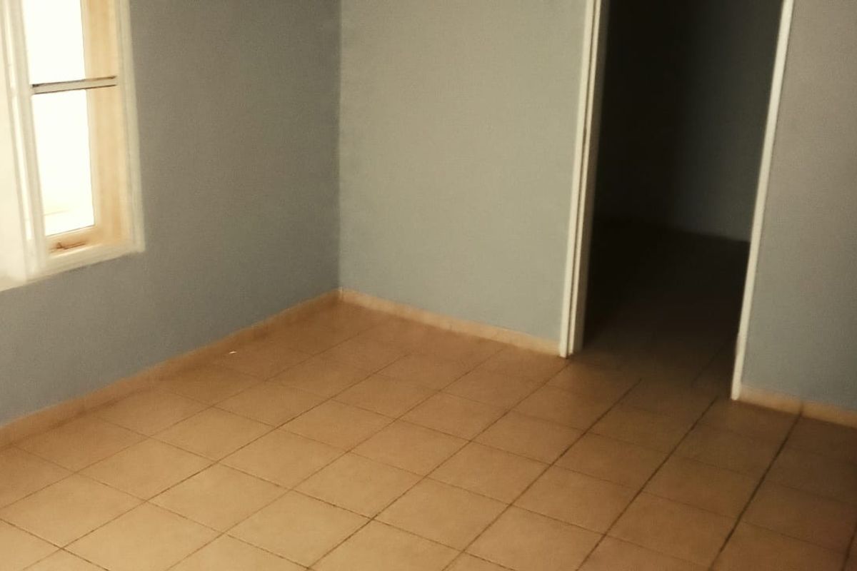 A vacant bedroom featuring tiled flooring, a window with natural light, and a wooden door leading to an adjacent space.