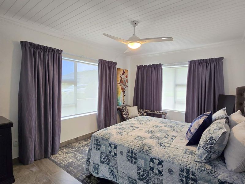 A well-lit bedroom featuring a tongue and groove ceiling, a central ceiling fan, and tiled flooring, offering a comfortable and functional living space.