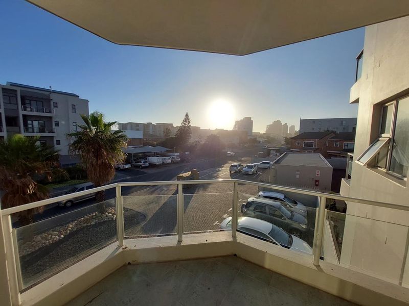 A private balcony featuring a glass balustrade and tiled flooring, offering an elevated view of the surrounding neighborhood and streetscape.