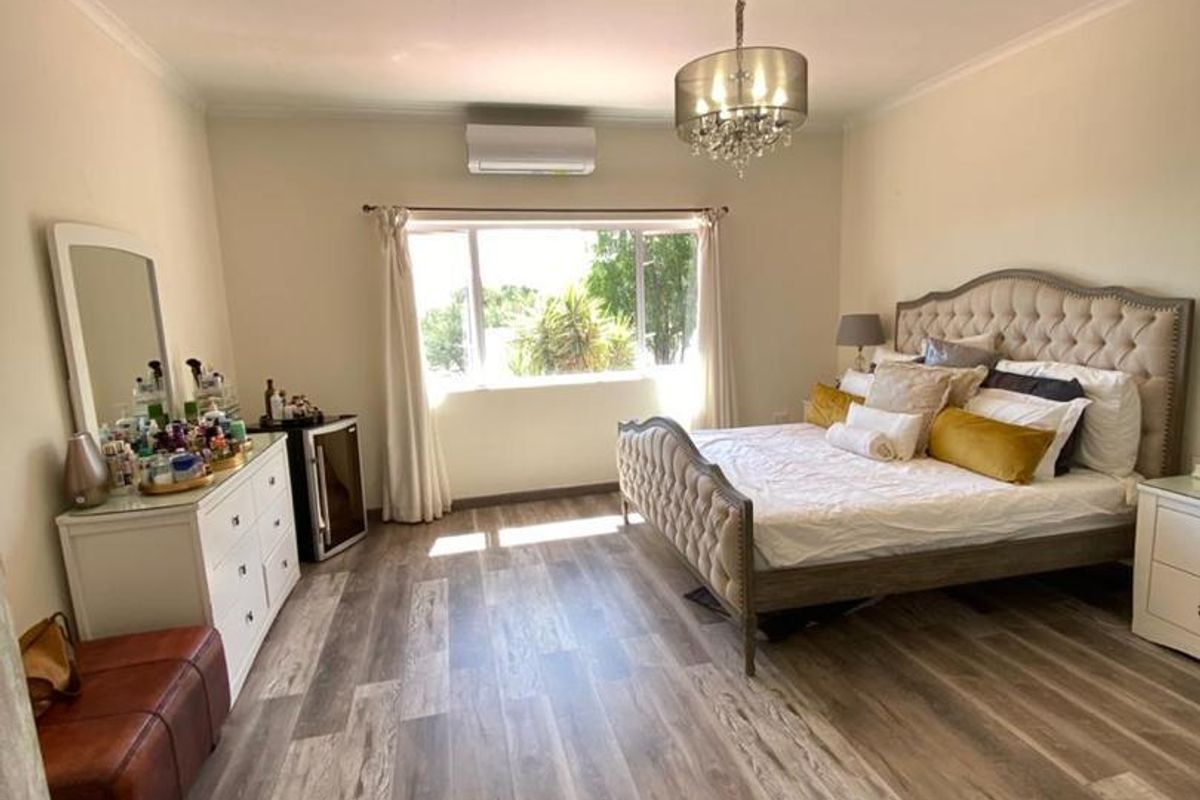 Spacious bedroom featuring modern laminate flooring, a split-system air conditioner, and elegant crown molding with a central chandelier.