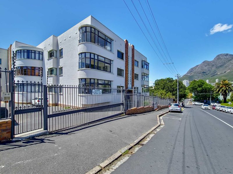 Street-level view of the apartment building facade featuring curved windows, secure metal fencing, and gated access.
