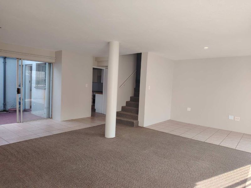 Spacious open-plan living area featuring a central structural column, staircase, and sliding glass doors leading to an outdoor space.