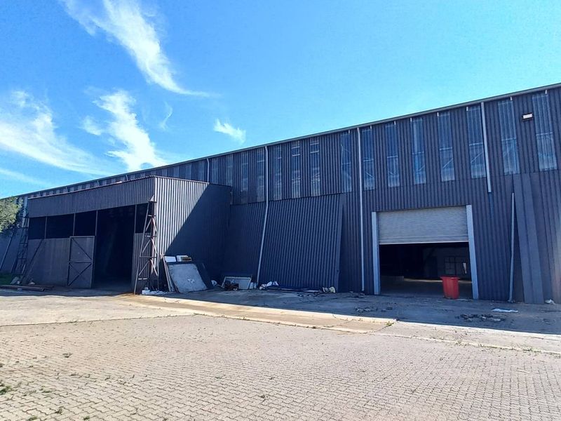 Industrial warehouse exterior featuring corrugated metal cladding, multiple roller shutter access doors, and a paved yard area.