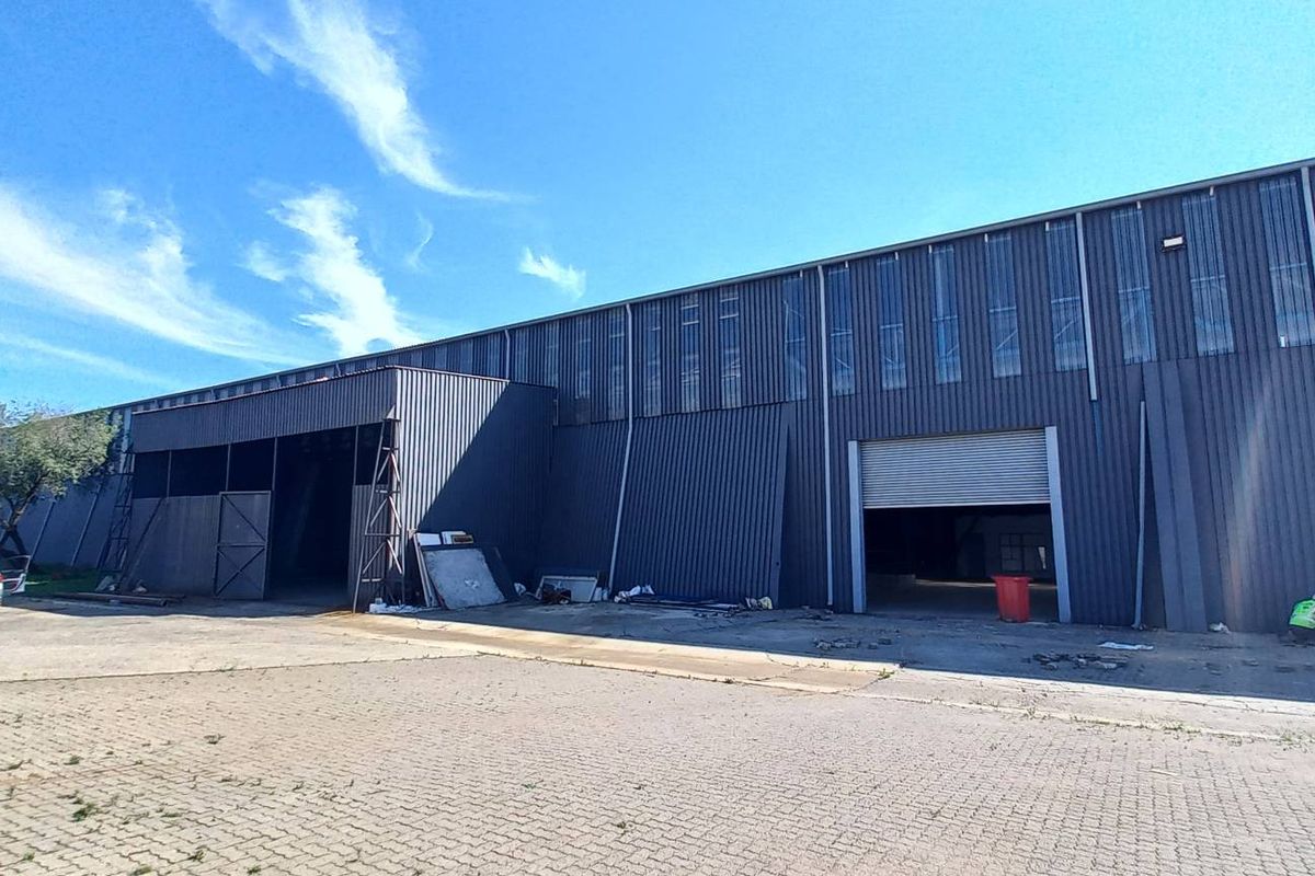 Industrial warehouse exterior featuring corrugated metal cladding, multiple roller shutter access doors, and a paved yard area.