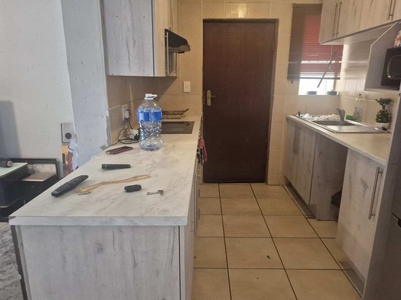 A functional kitchen featuring light wood-look cabinetry, laminate countertops, a built-in hob with extractor, and tiled flooring throughout.