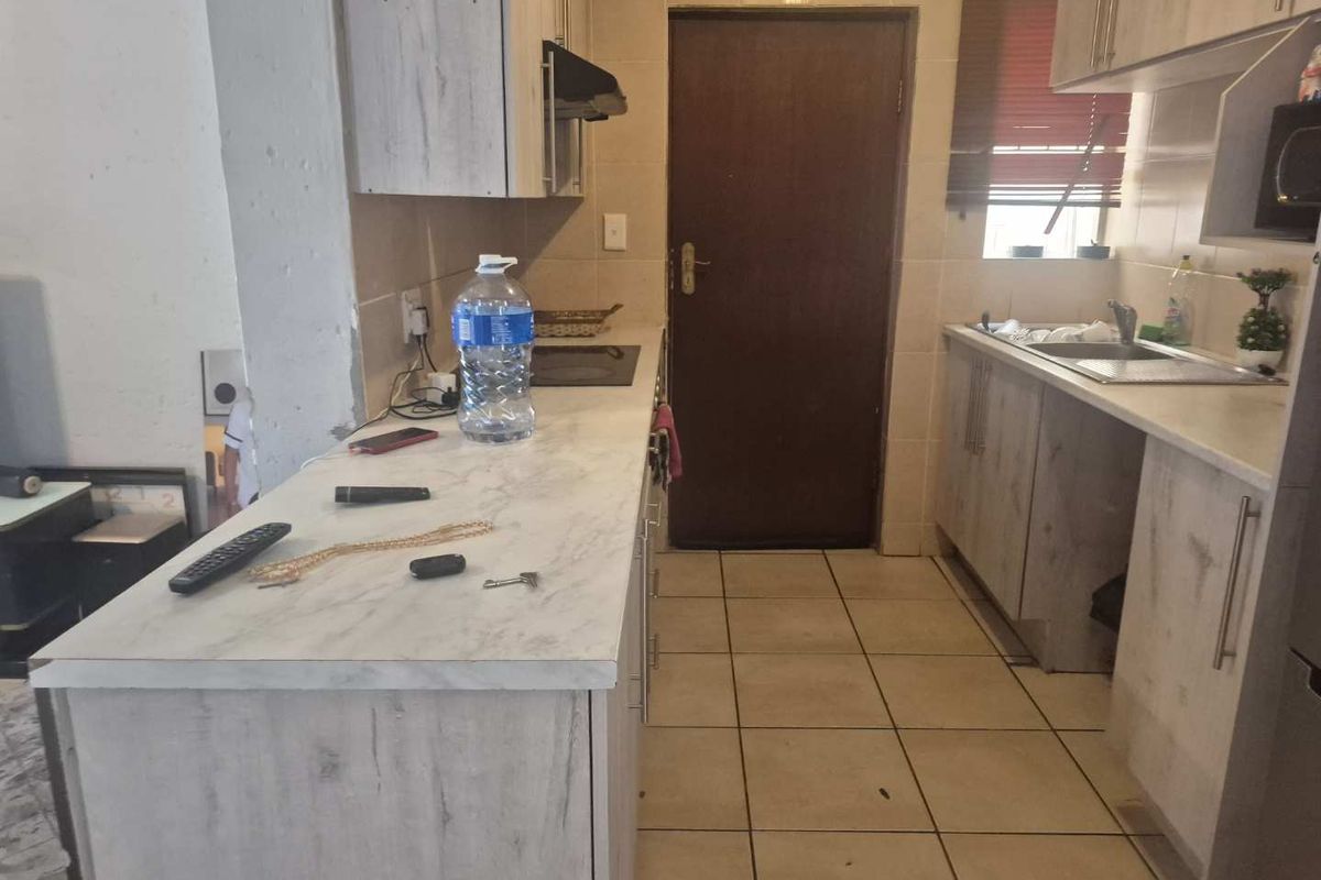 A functional kitchen featuring light wood-look cabinetry, laminate countertops, a built-in hob with extractor, and tiled flooring throughout.