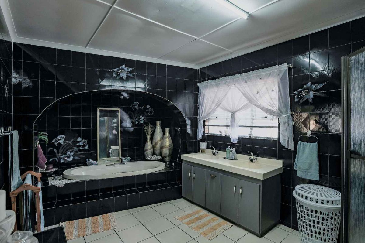 A spacious bathroom featuring a built-in bathtub set within a tiled alcove, a double vanity unit, and dark decorative wall tiling.