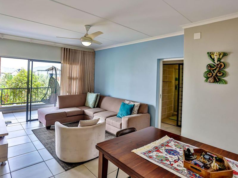 Open-plan living area featuring tiled floors, a ceiling fan, and direct access to a private balcony through sliding glass doors.