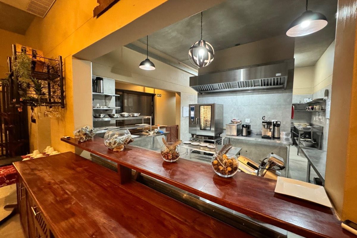 A professional-grade commercial kitchen featuring stainless steel prep surfaces, a built-in oven, an extractor hood, and a wooden service counter.