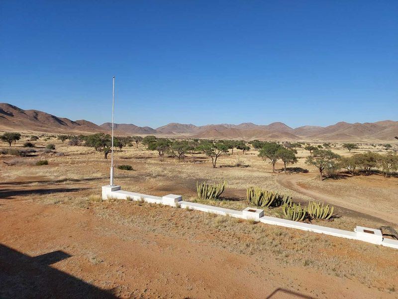 Expansive view of the arid farm landscape featuring a low masonry boundary wall and a flagpole set against a backdrop of distant mountains.