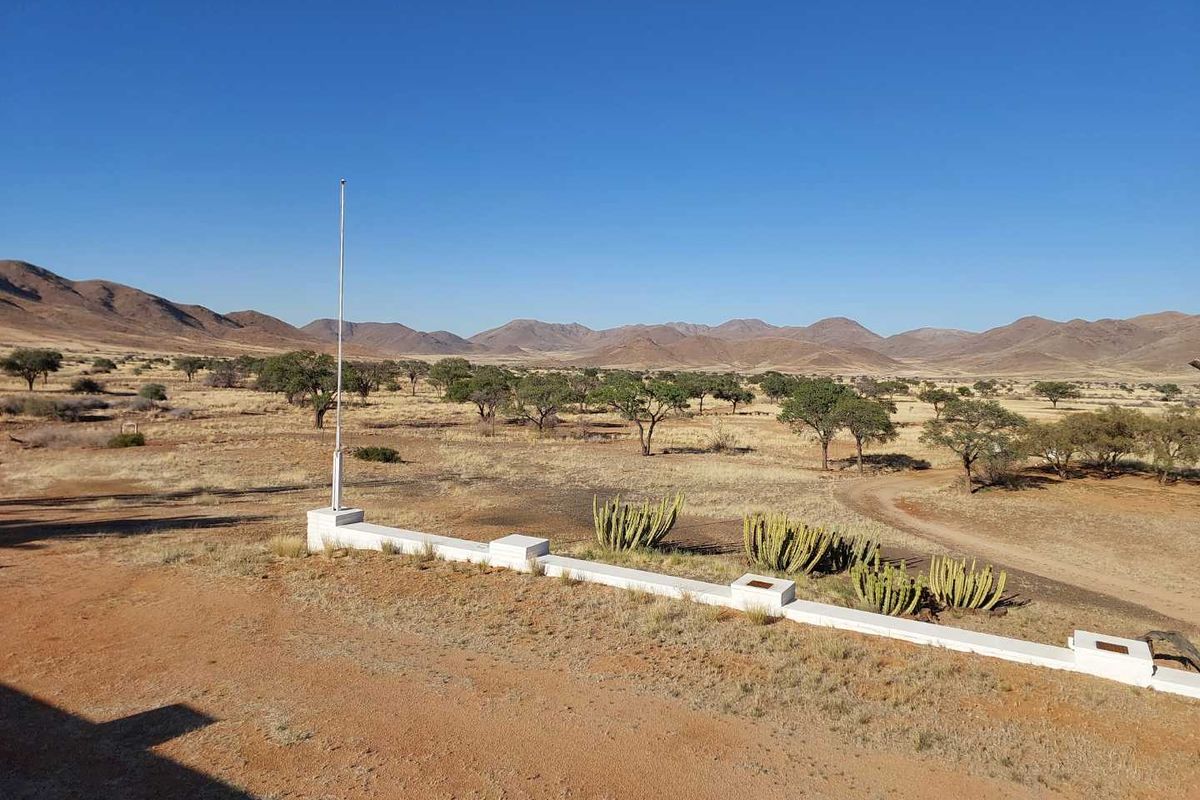 Expansive view of the arid farm landscape featuring a low masonry boundary wall and a flagpole set against a backdrop of distant mountains.