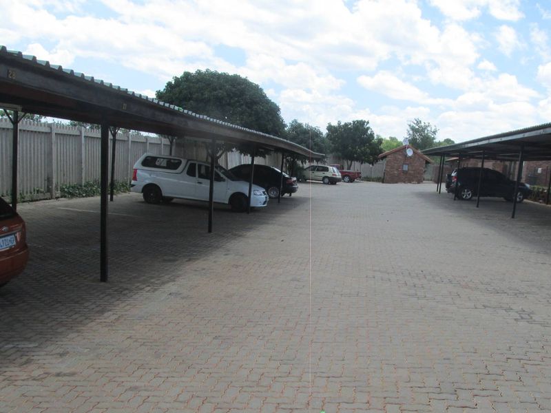 Outdoor parking area featuring covered parking bays with corrugated metal roofing and paved driveway surfaces within a secure complex.