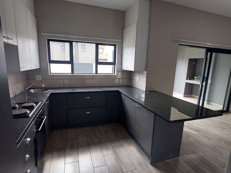 Modern kitchen featuring dark cabinetry, granite countertops, built-in oven and hob, tiled flooring, and direct access to an outdoor area via sliding doors.