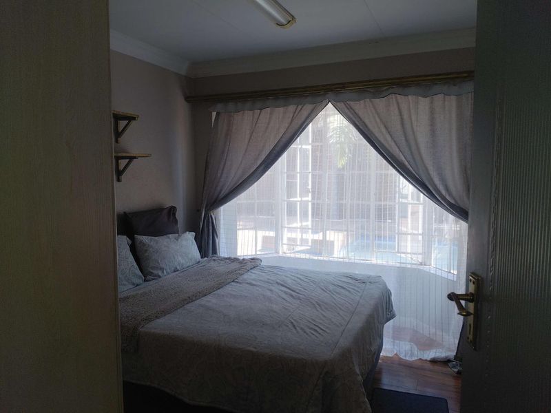 A bedroom featuring a large bay window, laminate flooring, and coving, offering a view towards the exterior pool area.
