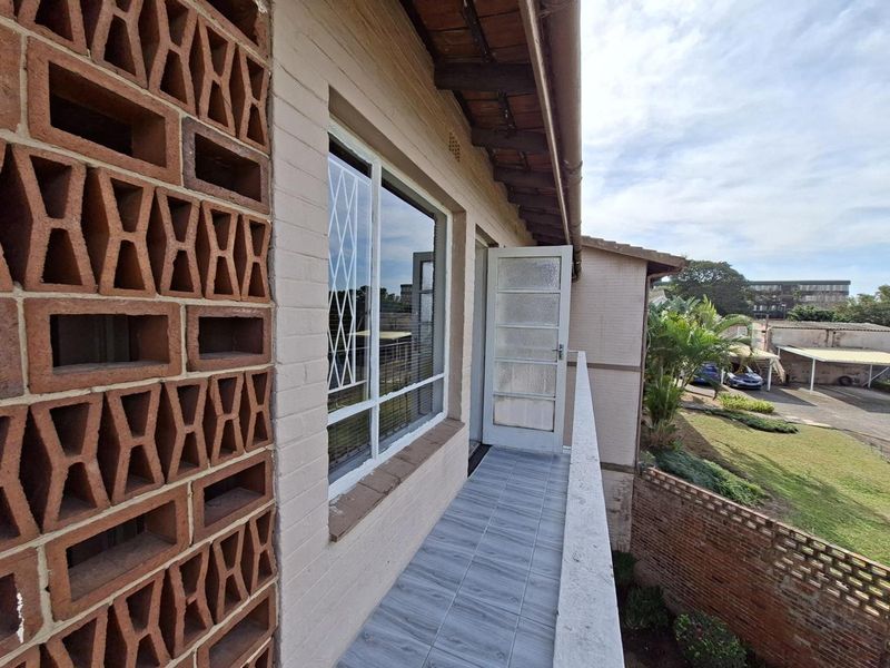 A balcony area featuring a decorative breeze block screen, tiled flooring, and a security gate, overlooking the apartment complex grounds.