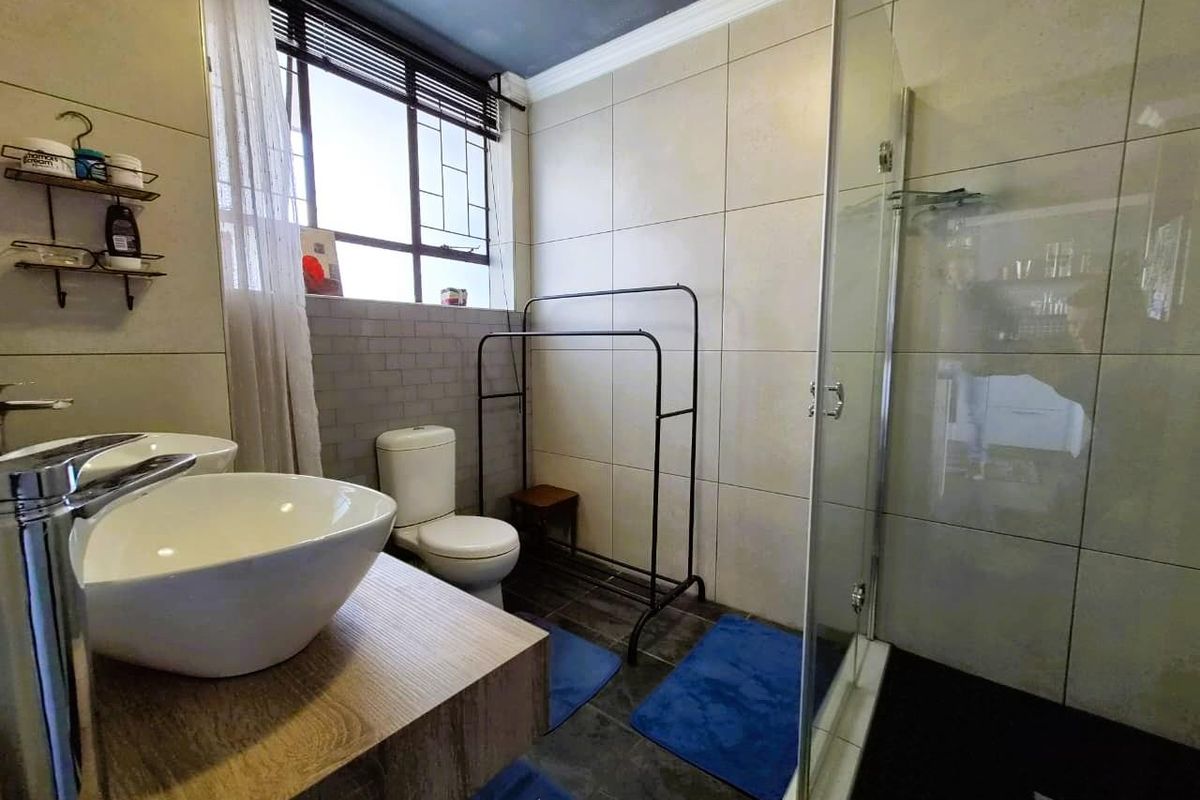 Modern bathroom featuring a glass-enclosed shower, dual vessel sinks on a wooden vanity, and large-format wall tiling.