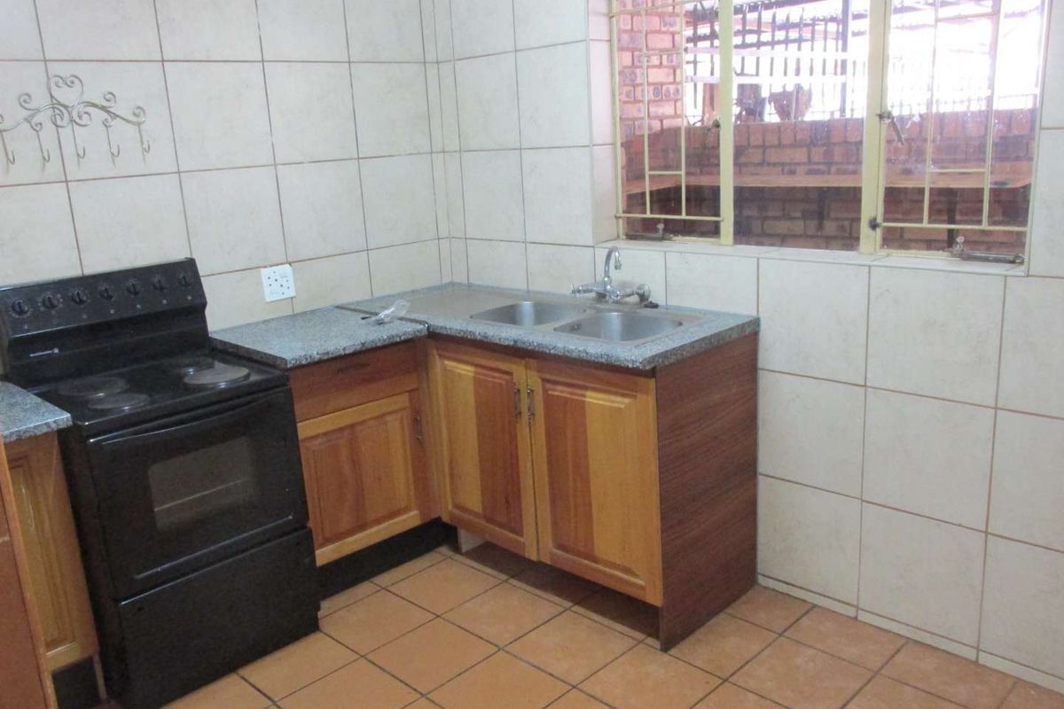 A functional kitchen featuring wooden cabinetry, granite countertops, a double bowl sink, and a freestanding stove, finished with tiled walls and flooring.