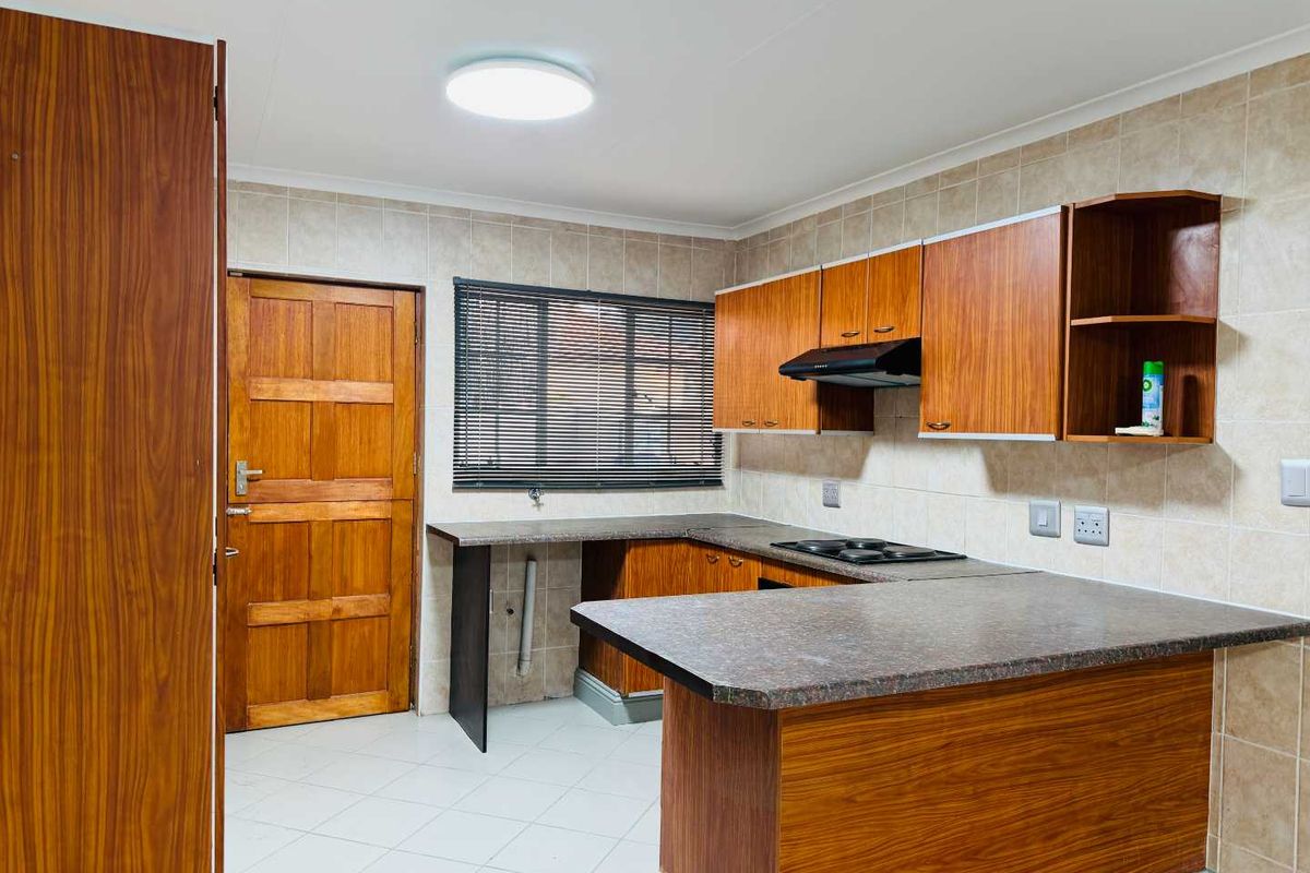A functional kitchen featuring wood-look laminate cabinetry, tiled backsplash, built-in hob with extractor fan, and a breakfast counter.