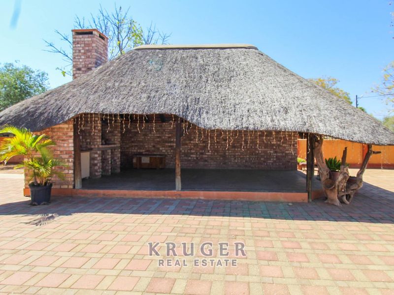 Outdoor entertainment area featuring a thatched roof, brick fireplace, and built-in braai, set on a paved patio.