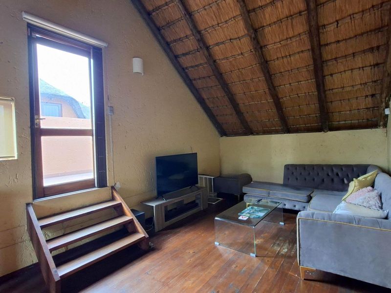Cozy living area featuring a unique thatched roof with exposed timber rafters, wooden flooring, and direct access to an outdoor space via a glass door.