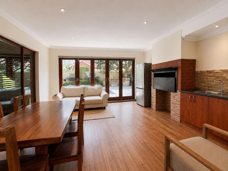 Open-plan living area featuring laminate flooring, a built-in braai, kitchenette cabinetry with sink, and large sliding doors opening to the rear patio.
