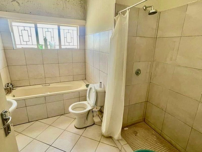 A dated bathroom featuring a bathtub, separate shower, and toilet, currently requiring significant maintenance and cosmetic updates to the wall finishes.