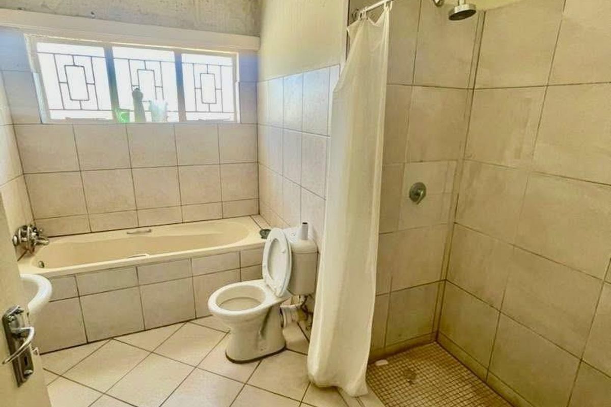 A dated bathroom featuring a bathtub, separate shower, and toilet, currently requiring significant maintenance and cosmetic updates to the wall finishes.
