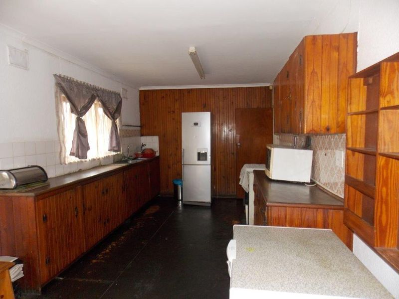 A dated kitchen featuring extensive wooden cabinetry, wood-paneled walls, and laminate countertops, offering significant potential for a modern renovation.