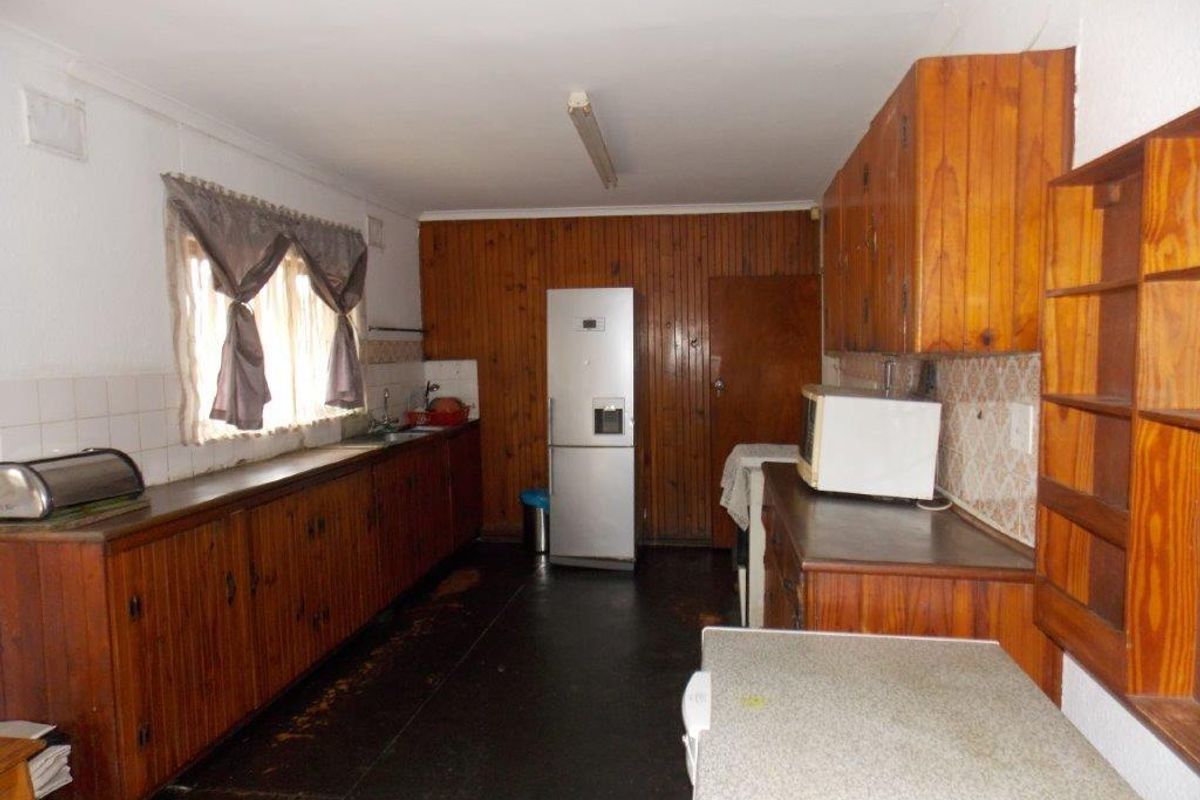 A dated kitchen featuring extensive wooden cabinetry, wood-paneled walls, and laminate countertops, offering significant potential for a modern renovation.