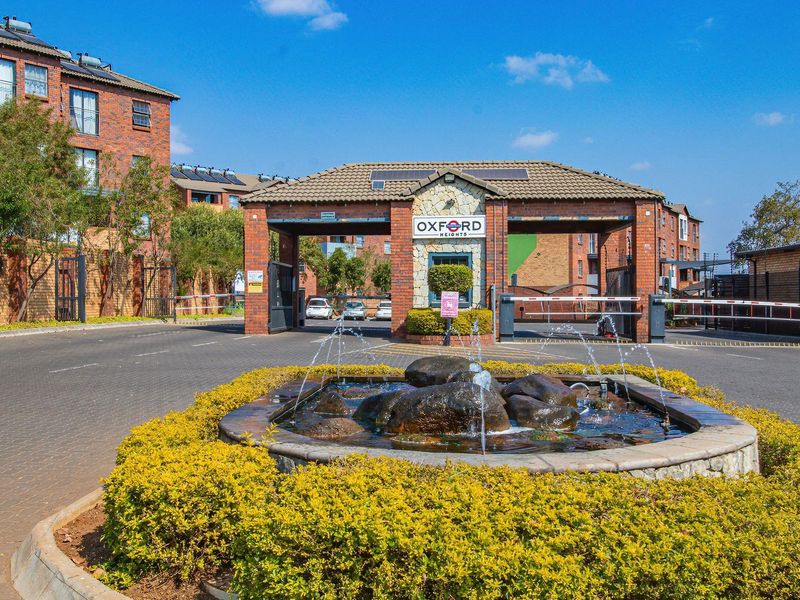The main entrance to Oxford Heights apartment complex, featuring a secure gatehouse, boom gates, and a decorative water fountain in the driveway.