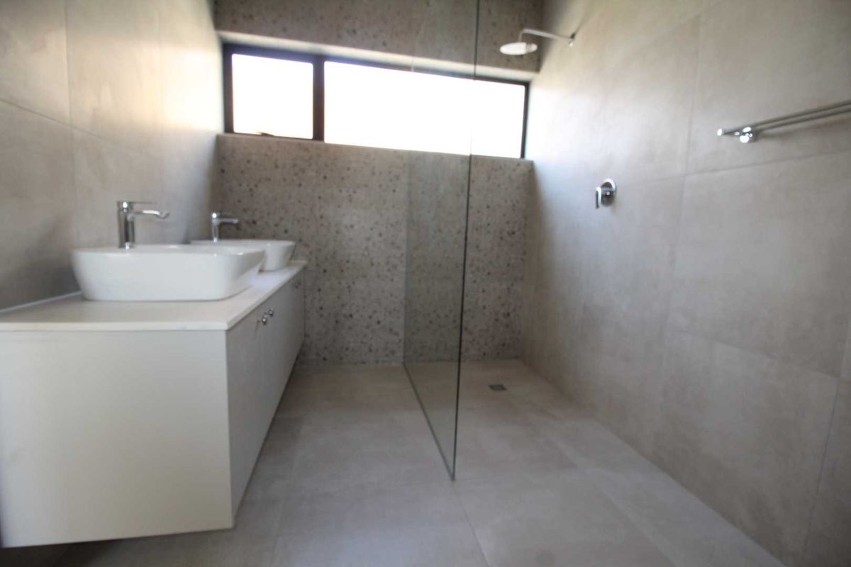 Modern bathroom featuring a double vanity, walk-in shower with glass screen, and contemporary neutral tiling.