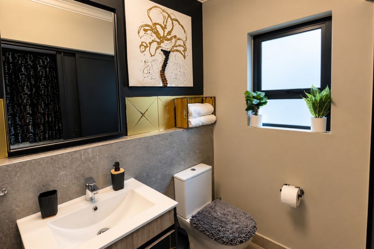 A modern bathroom featuring a vanity with a ceramic basin, chrome mixer tap, wall-mounted mirror, and a toilet with a frosted glass window.