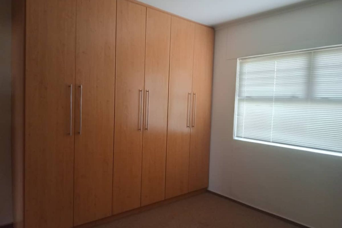 A bedroom featuring wall-to-wall built-in wooden cabinetry and a window fitted with horizontal blinds.