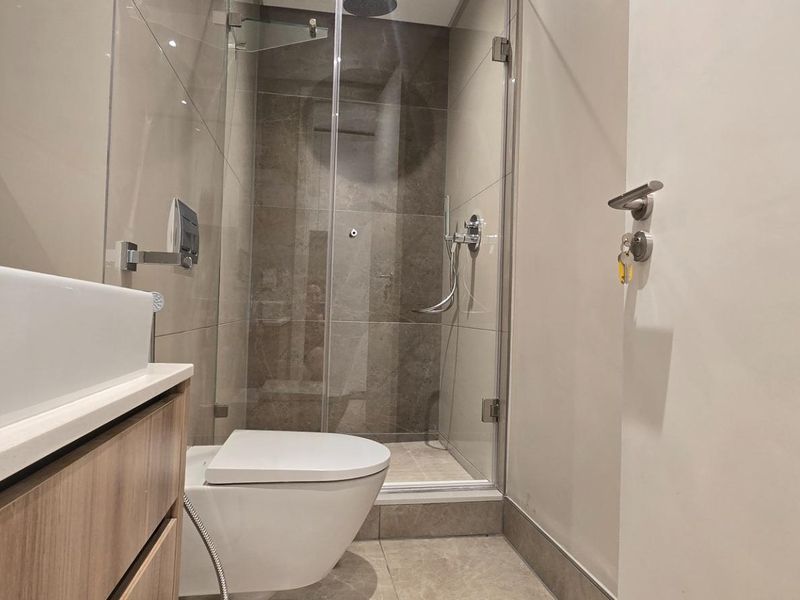 Modern bathroom featuring a wall-mounted toilet, a glass-enclosed shower with a rain shower head, and a sleek vanity with a countertop basin.