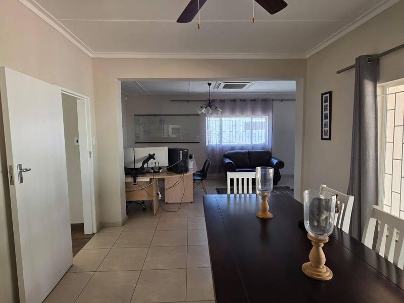 Open plan living and dining area featuring tiled flooring, ceiling fan, and large windows with security bars, providing a functional and connected living space.