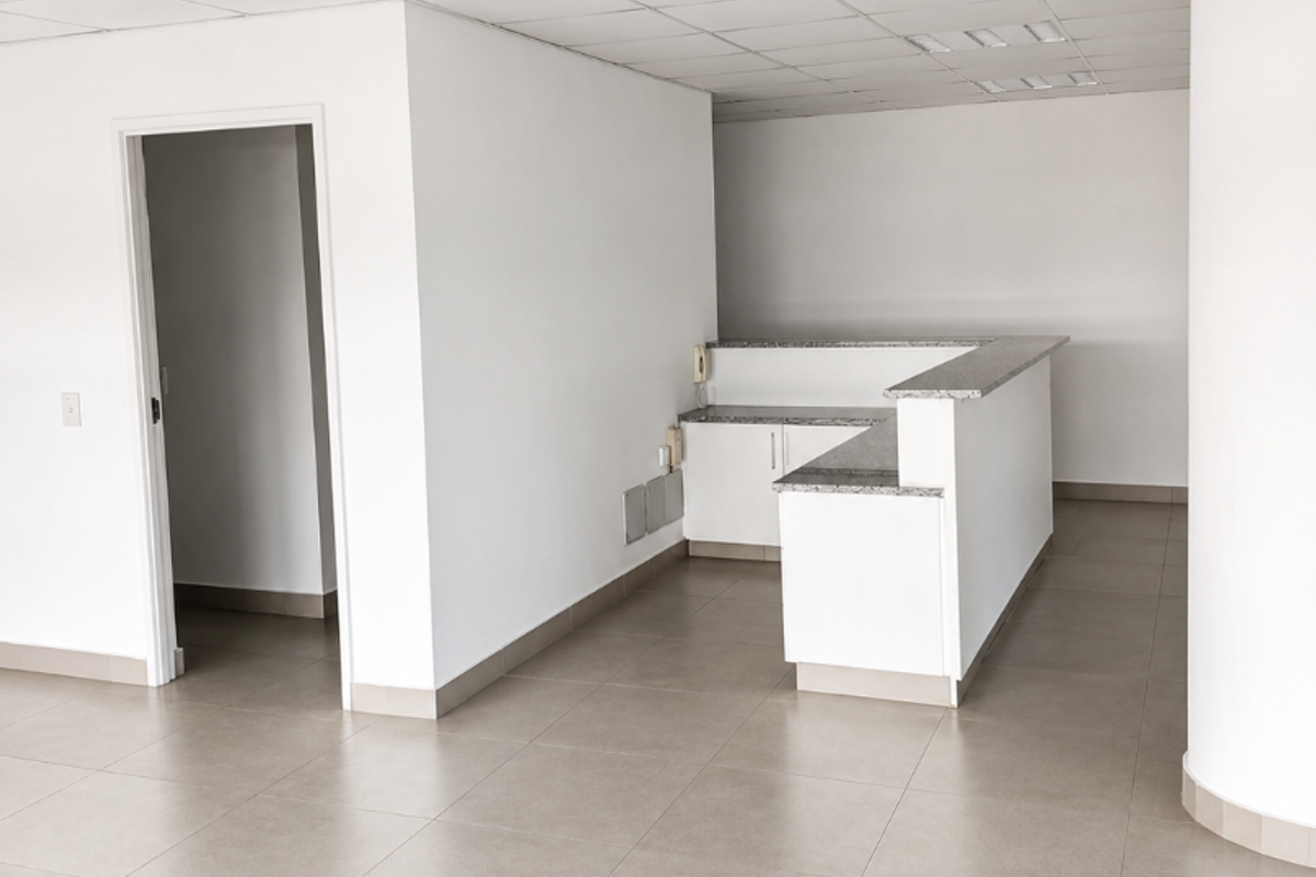 An empty office space featuring a built-in reception desk, tiled flooring, and a suspended ceiling with recessed lighting.