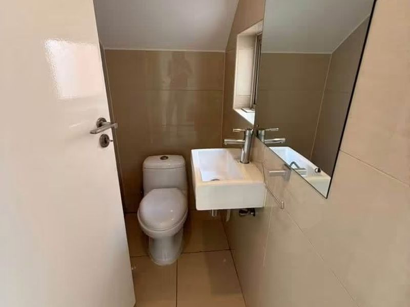 A compact, modern guest bathroom featuring tiled walls and flooring, a wall-mounted basin with a mixer tap, and a large mirror.