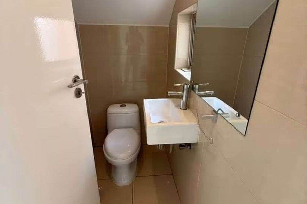 A compact, modern guest bathroom featuring tiled walls and flooring, a wall-mounted basin with a mixer tap, and a large mirror.