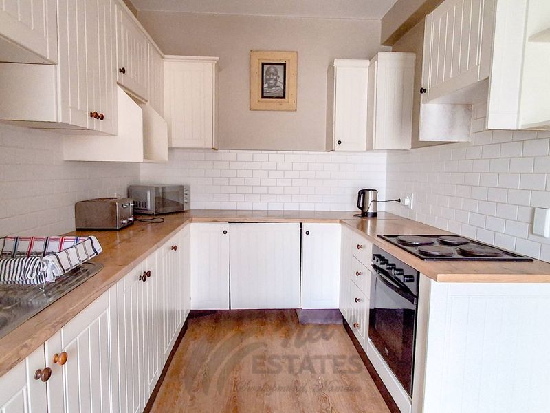 A functional U-shaped kitchen featuring white cabinetry, subway tile backsplash, wooden countertops, and integrated electric cooking appliances.