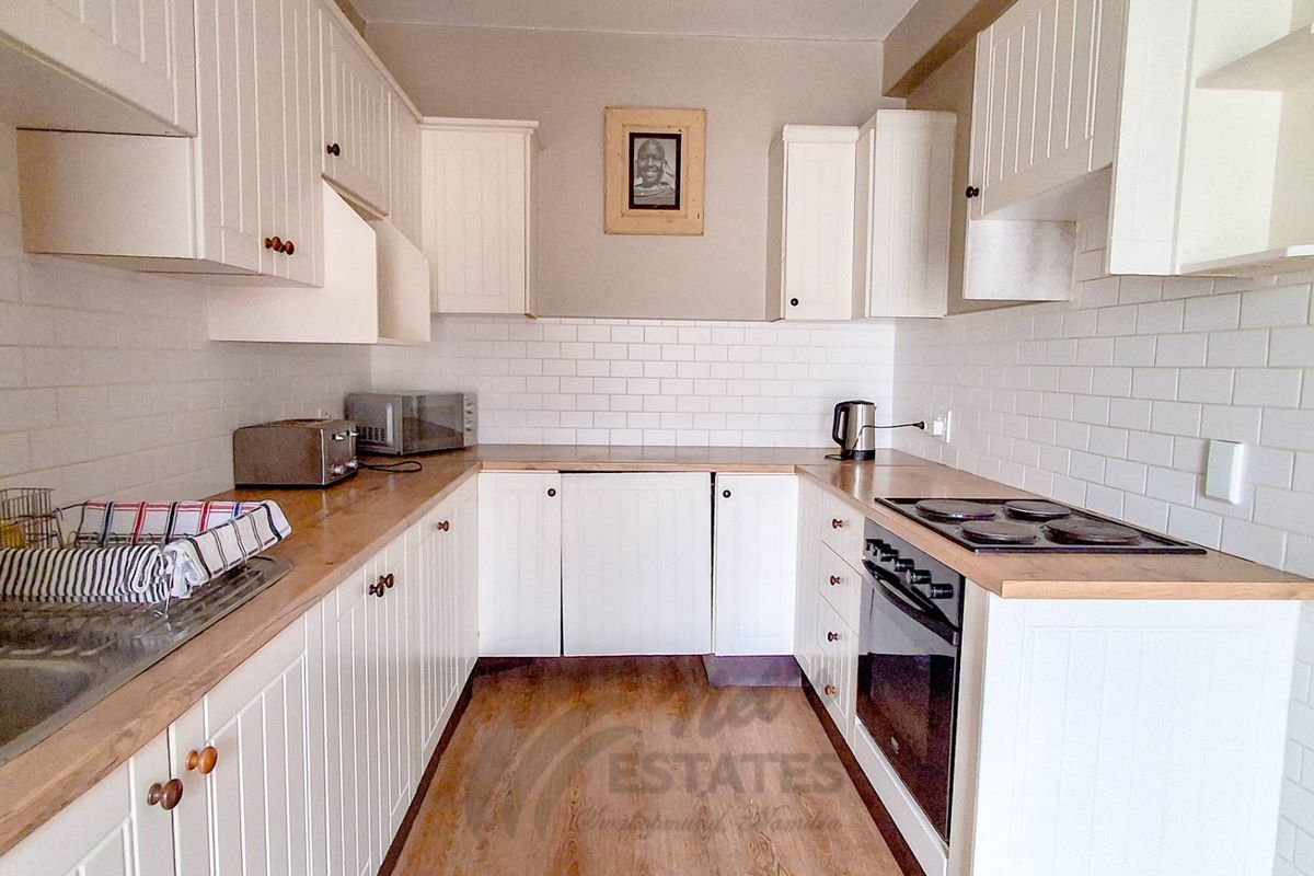 A functional U-shaped kitchen featuring white cabinetry, subway tile backsplash, wooden countertops, and integrated electric cooking appliances.
