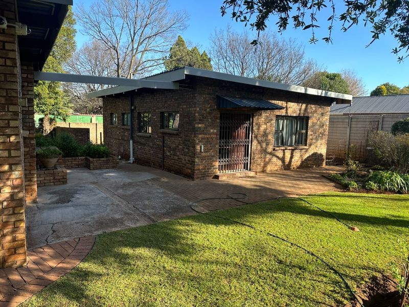 Rear view of a face brick house featuring a paved patio area, security gate, and established garden space.