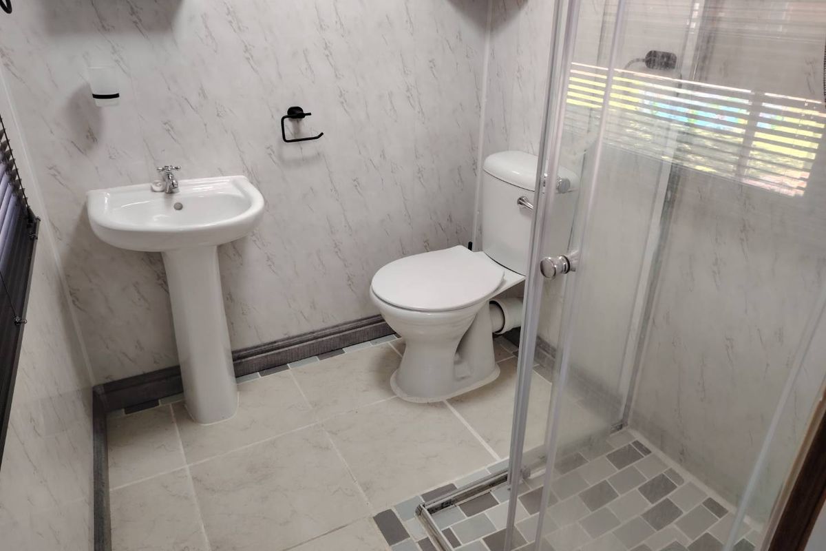A clean, functional bathroom featuring a pedestal washbasin, toilet, and a glass-enclosed shower with modern tiled finishes.