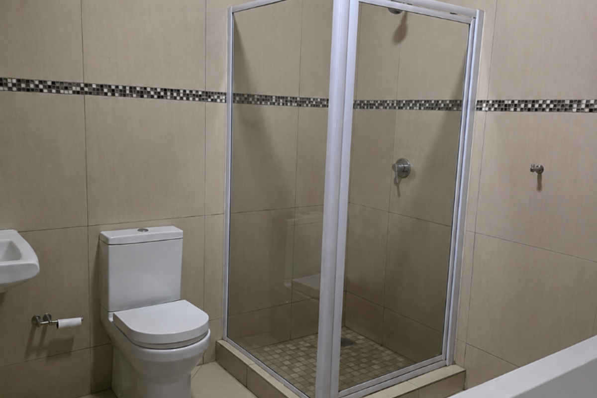 A clean, neutral-toned bathroom featuring a glass shower enclosure, a bathtub, and a modern toilet with full-height wall tiling.