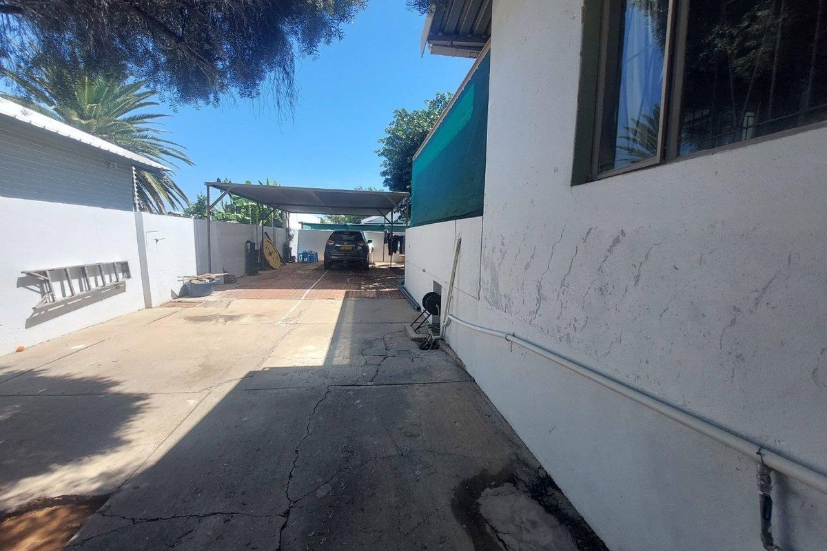 Side exterior view of the property featuring a concrete driveway, a carport structure, and perimeter boundary walls.