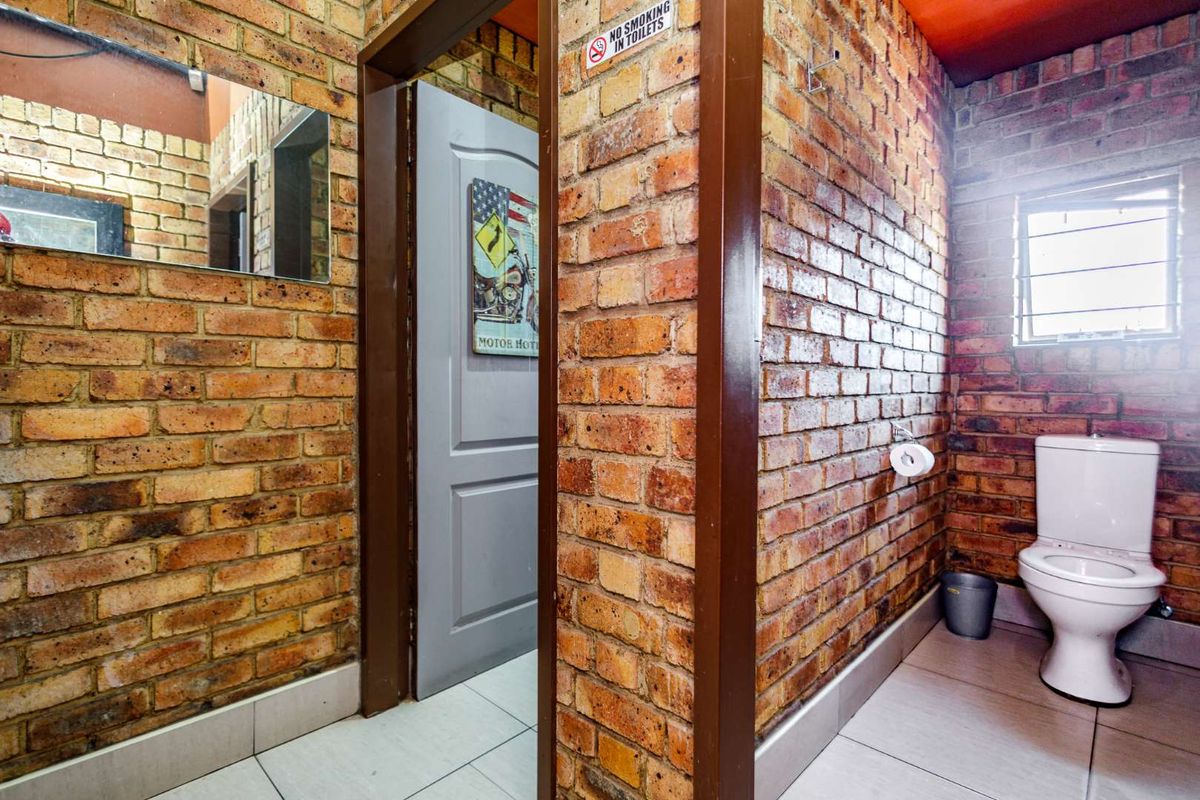 A functional restroom featuring exposed brick walls, tiled flooring, and a standard toilet suite.