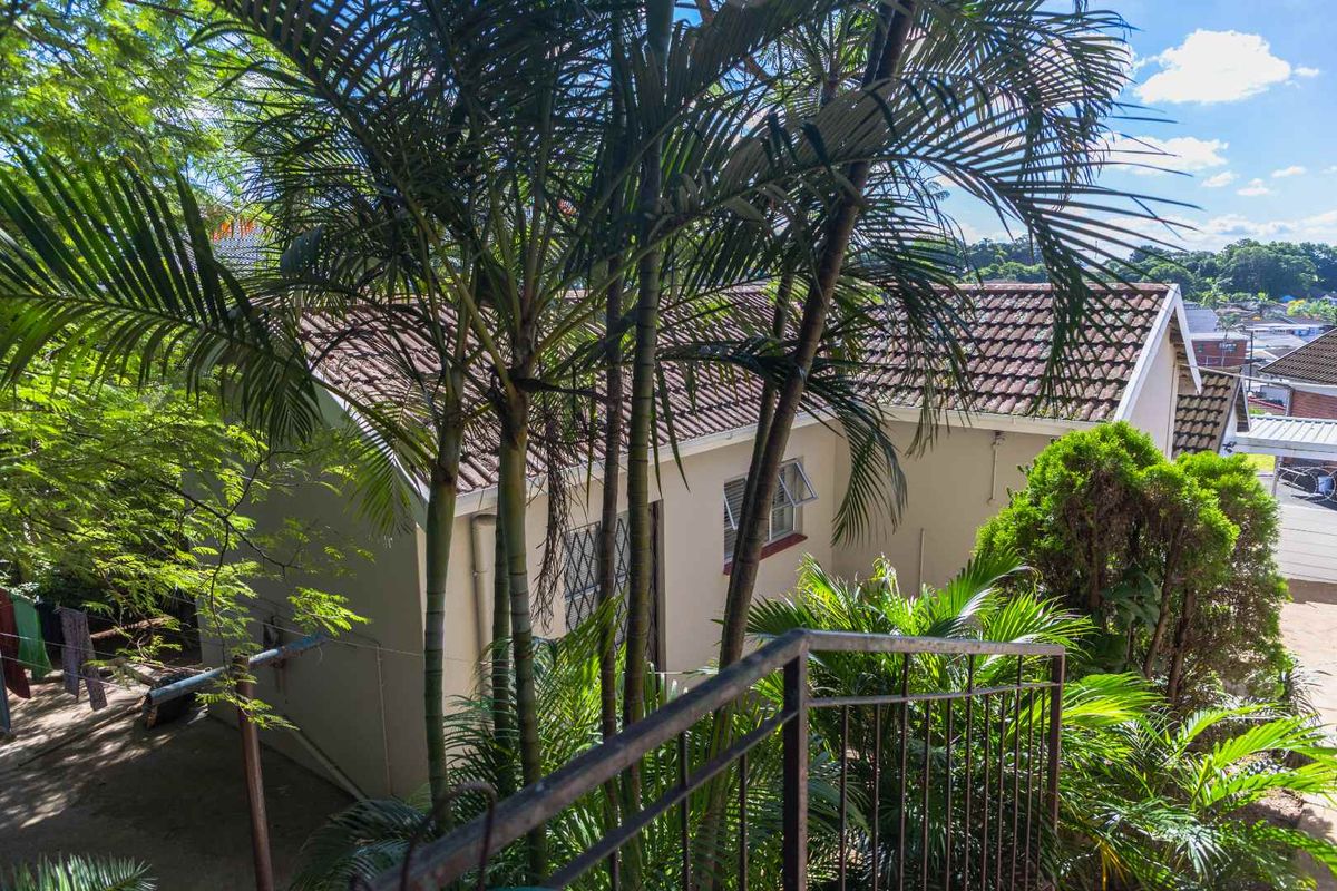 An elevated view of the property's rear exterior, featuring a tiled roof, established garden foliage, and metal security railings.