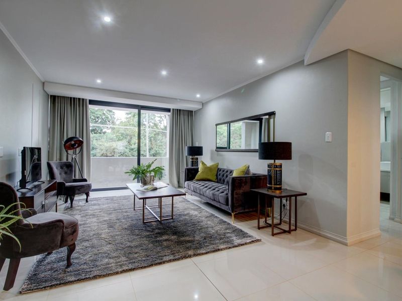 A well-maintained living room featuring modern recessed downlights, sleek tiled flooring, and a large sliding glass door providing access to the balcony.